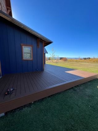 Blue house exterior with a wooden deck overlooking an open grassy field under a clear sky