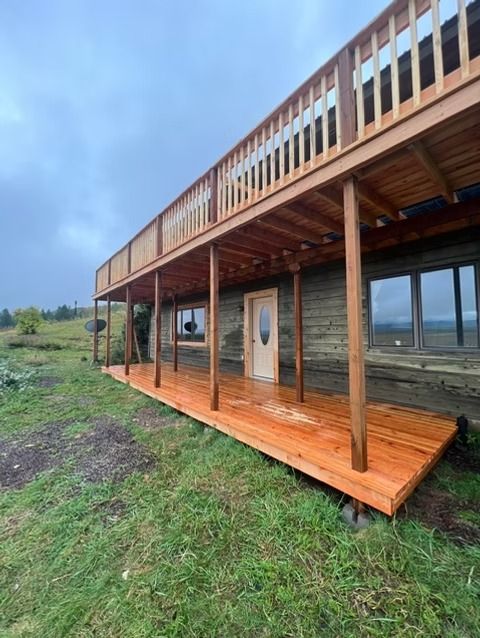 Wooden stilt cabin with a covered deck on a grassy hillside under a cloudy sky