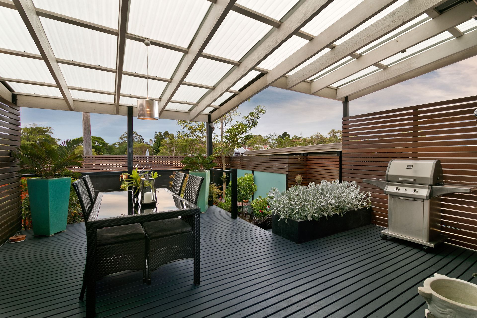 Modern rooftop patio with outdoor seating, grill, planters, and city view under a covered pergola