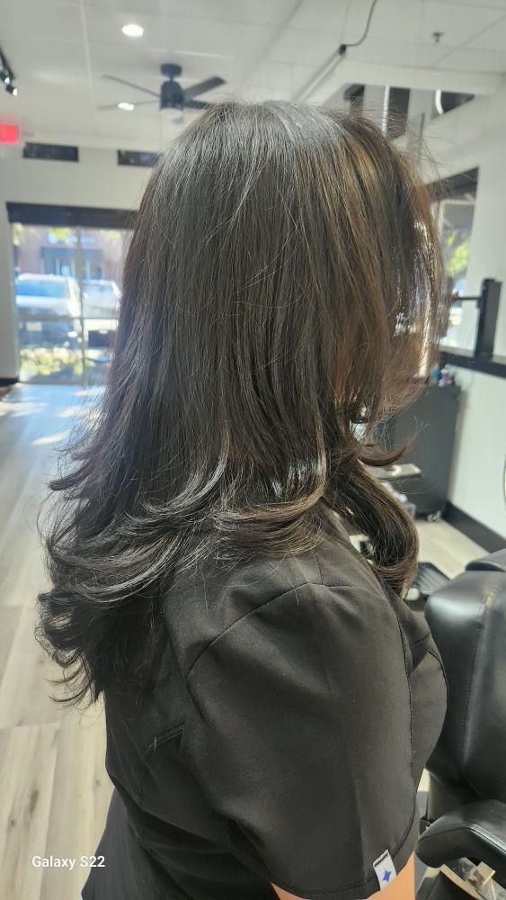 Woman with dark layered hair in a salon setting, wearing a black top.