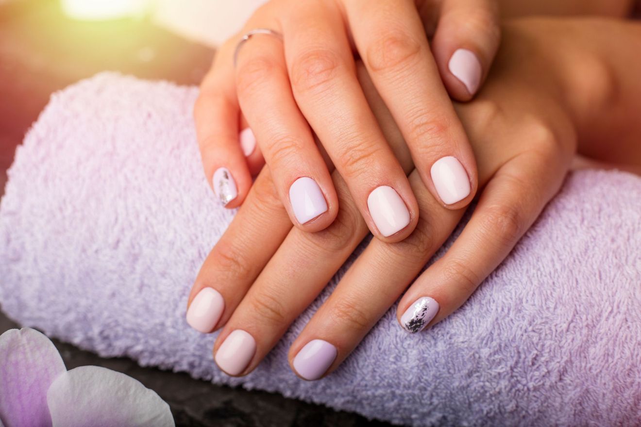 Hands with pale pink manicure resting on a rolled white towel in a spa setting
