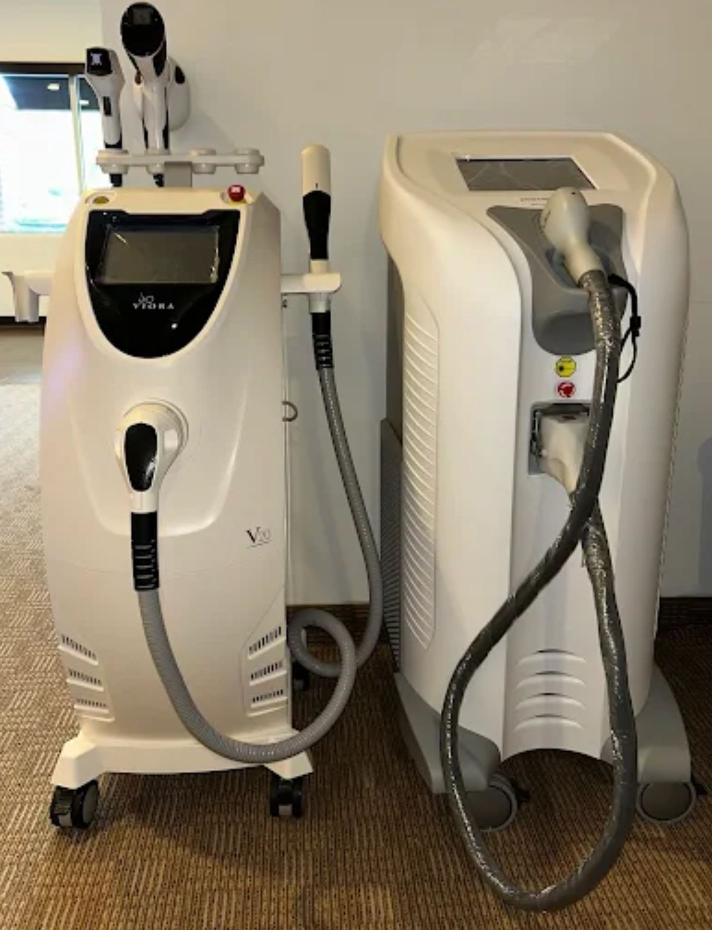 Two white medical laser machines with attached applicators on wheels in a room.