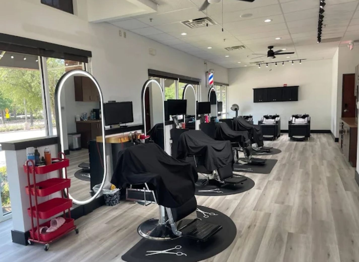 Interior of a barbershop with chairs covered in black capes and a red rolling cart.