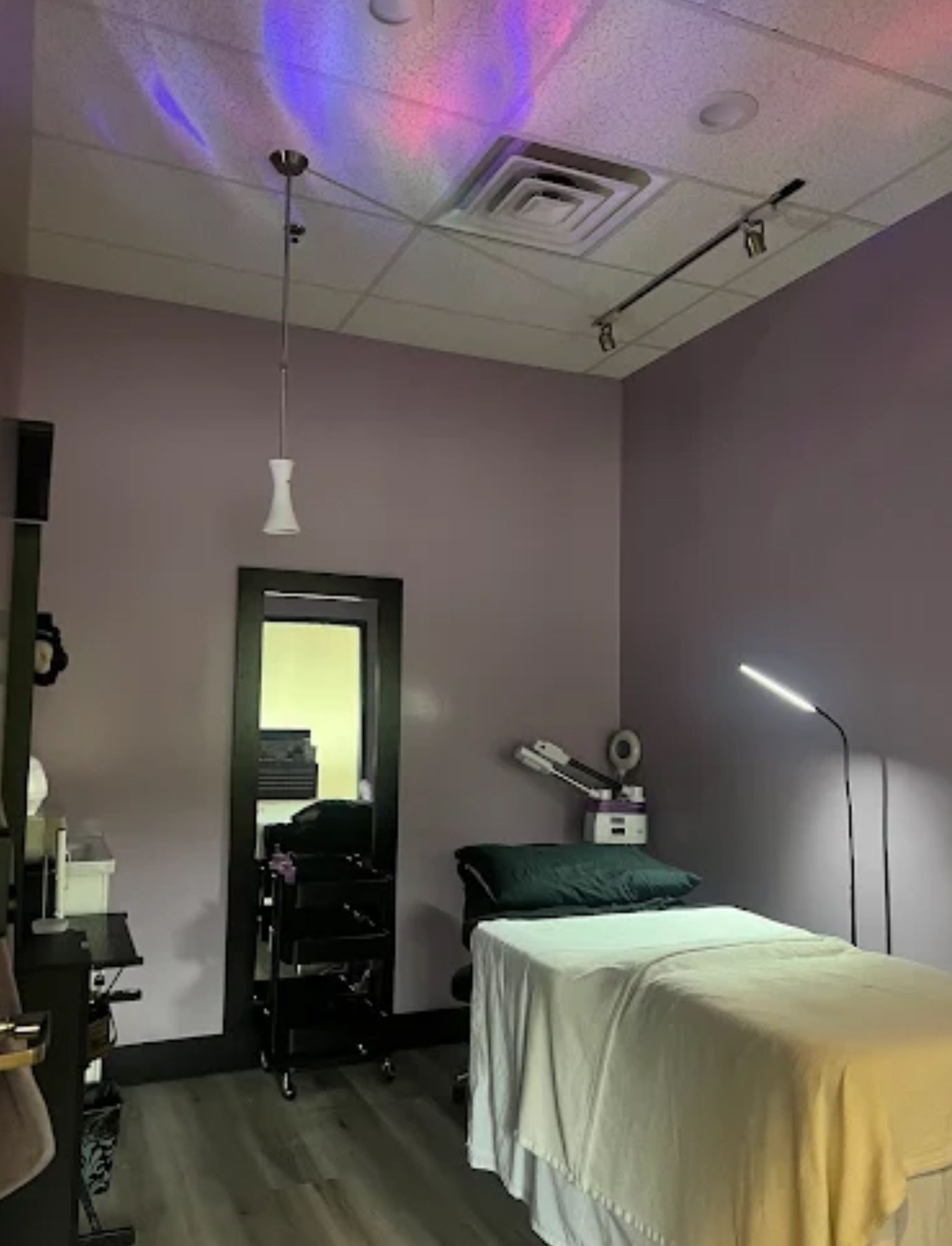 A spa treatment room with a bed covered in white sheets, purple walls, and decorative lighting.