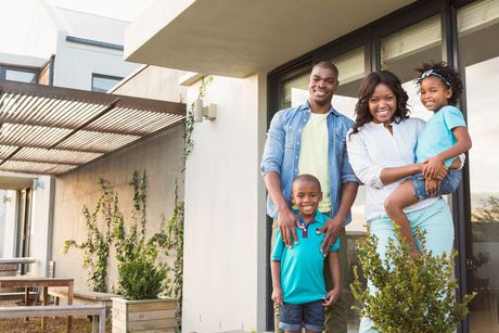 mom and dad with two kids in front of a home smiling.