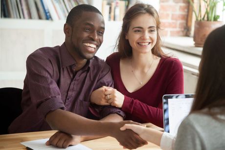 A man and a woman are shaking hands while sitting at a desk.