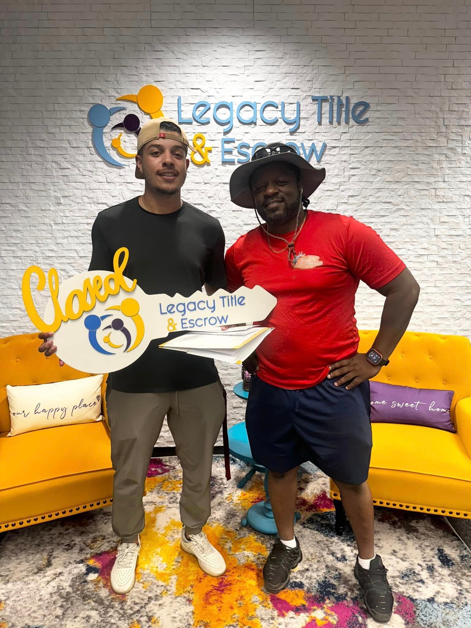 Two men are standing next to each other in a living room holding keys.