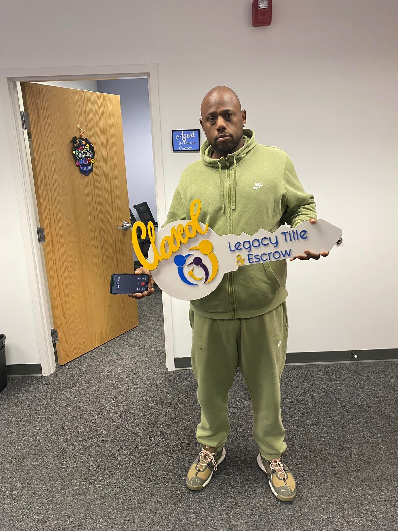A man in a green hoodie is holding a large key in front of a door.