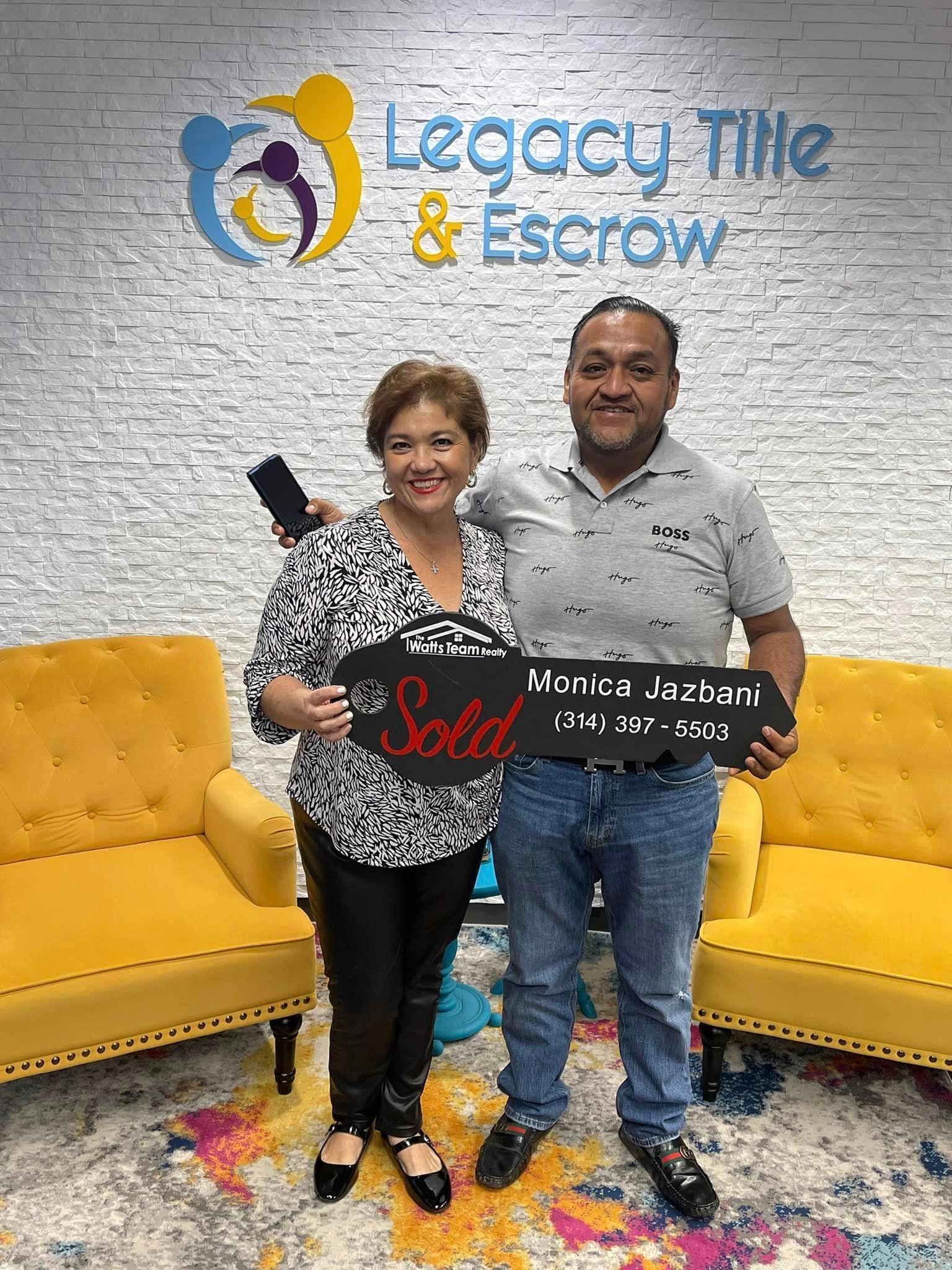 A man and a woman are standing next to each other holding a sold sign.