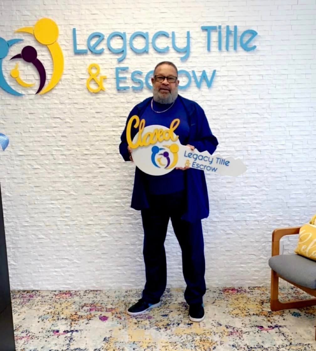A man holding a key in front of a wall that says legacy title & escrow