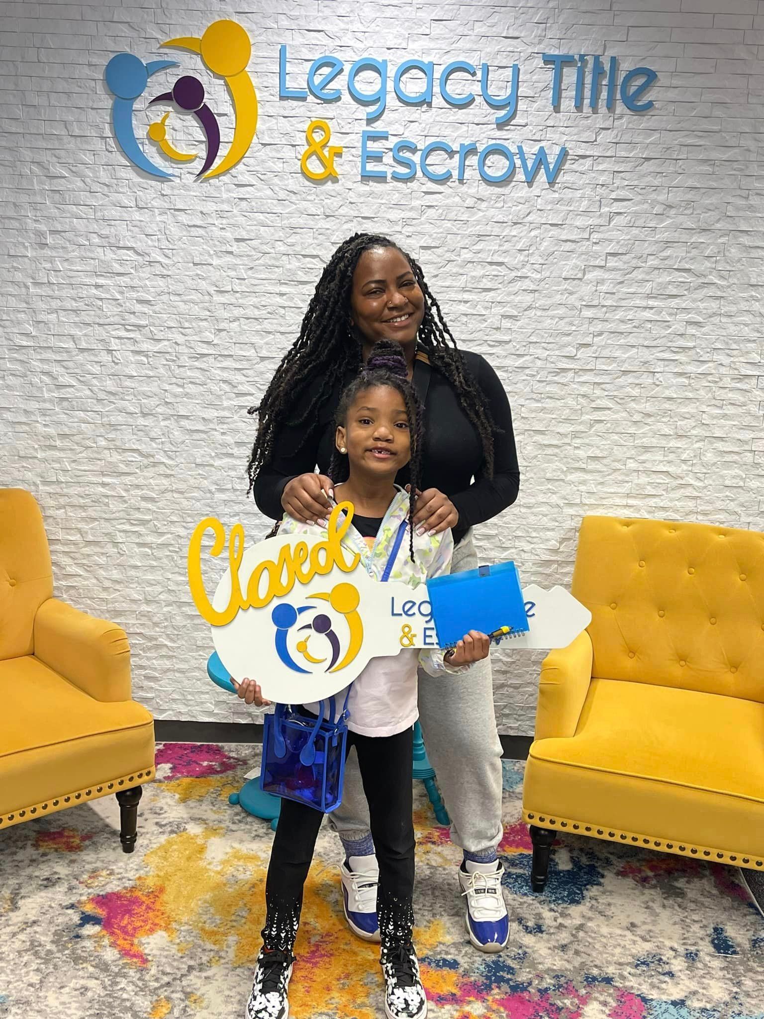 A woman and a little girl are holding keys in front of a legacy title & escrow sign.