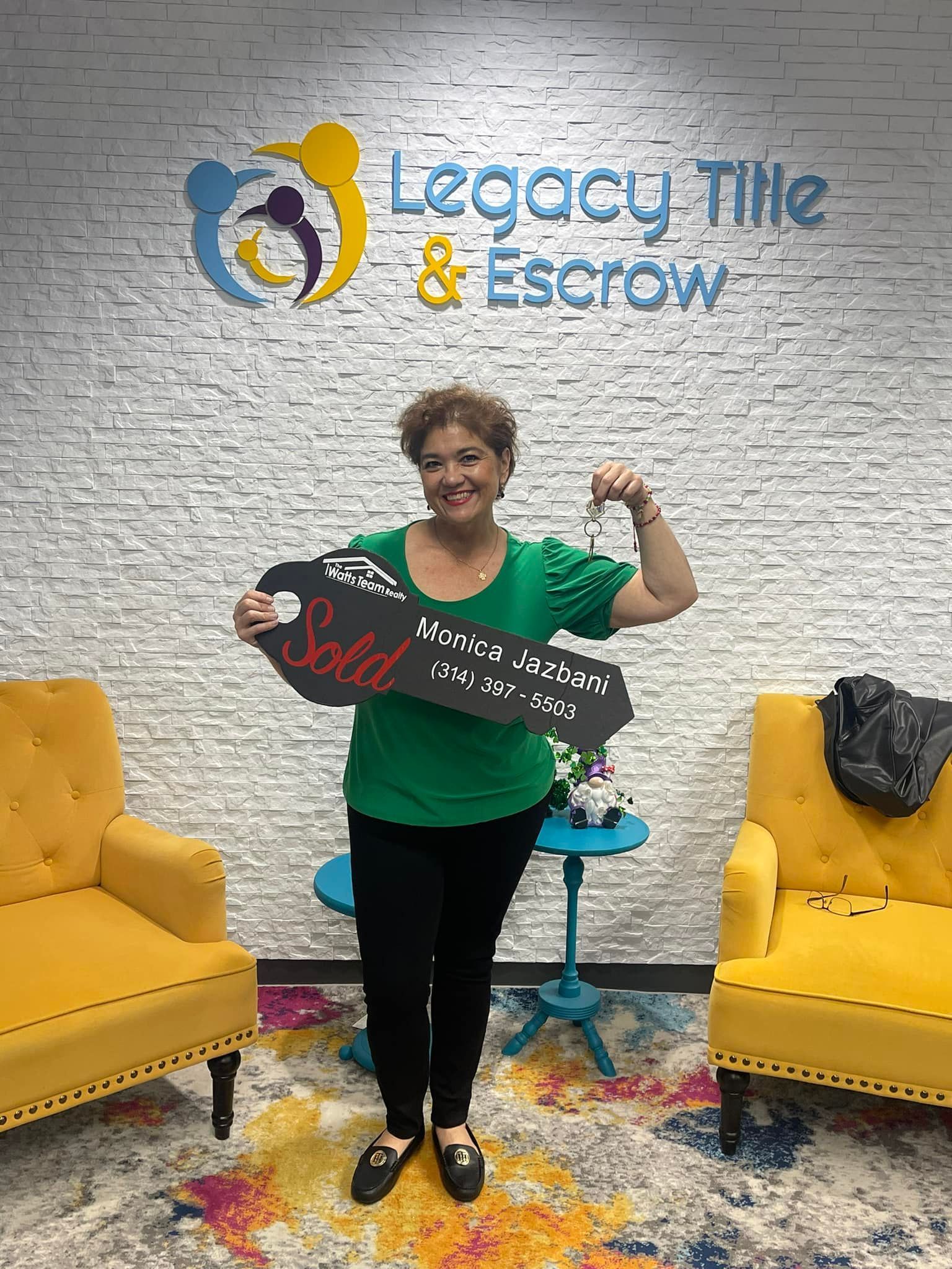 A woman is holding a key in front of a legacy tile and escrow sign.