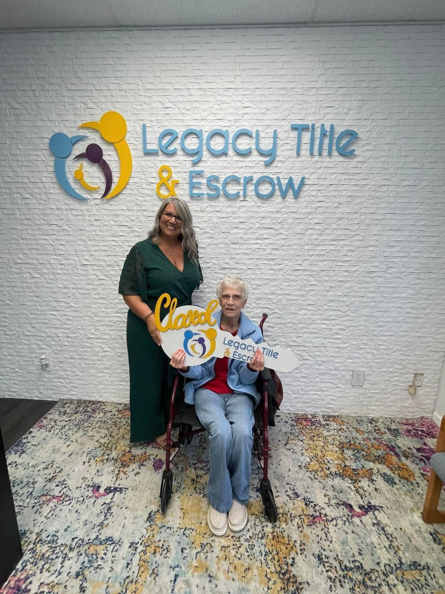 A woman is standing next to an elderly woman in a wheelchair holding a sign.