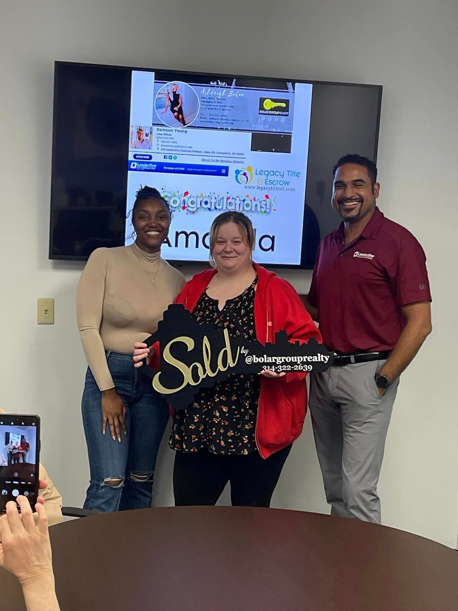 A group of people standing around a table holding a sign that says `` sold ''.