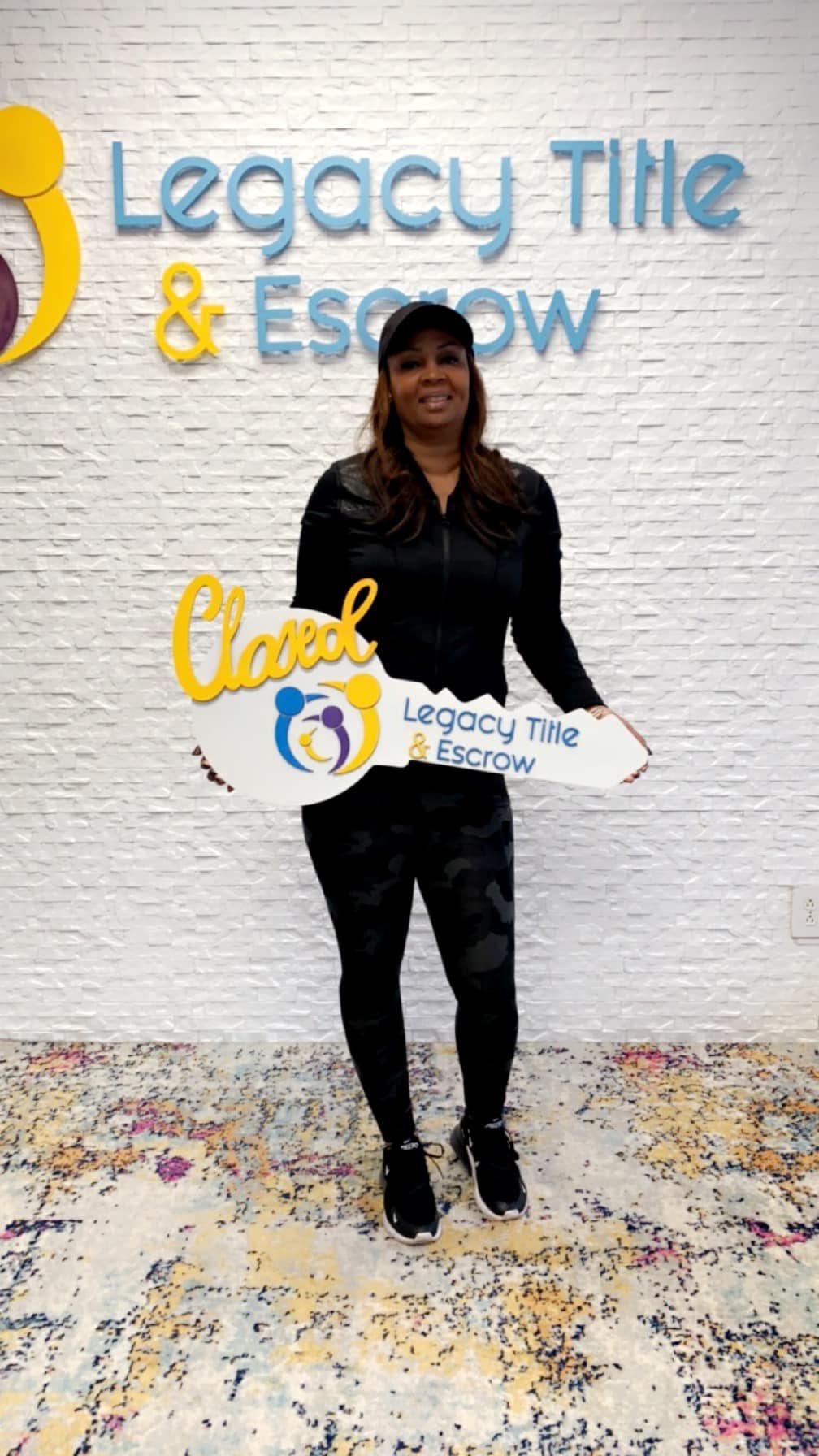 A woman is holding a key in front of a legacy title and escrow sign.