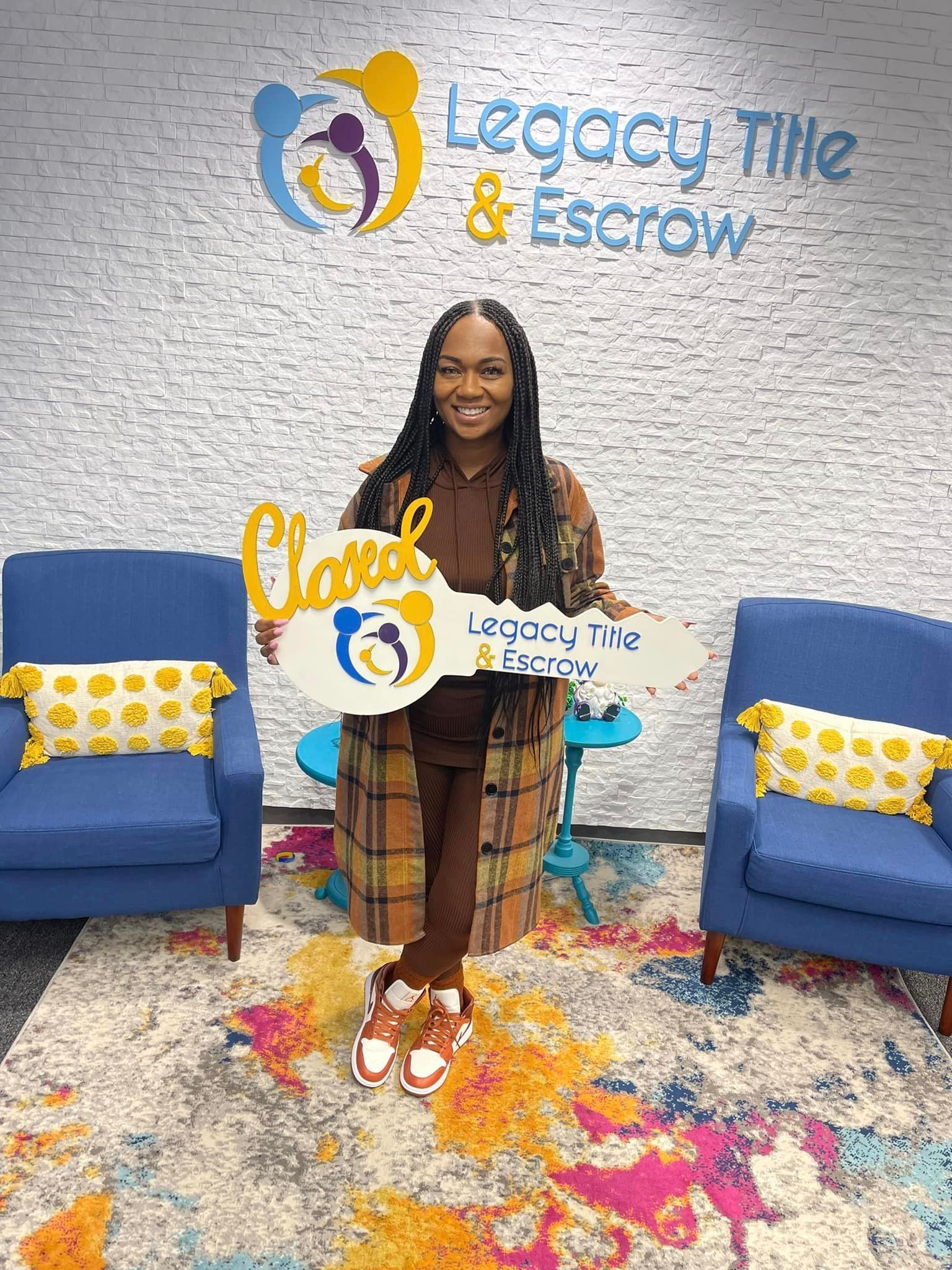 A woman is holding a key in front of a legacy title and escrow sign.