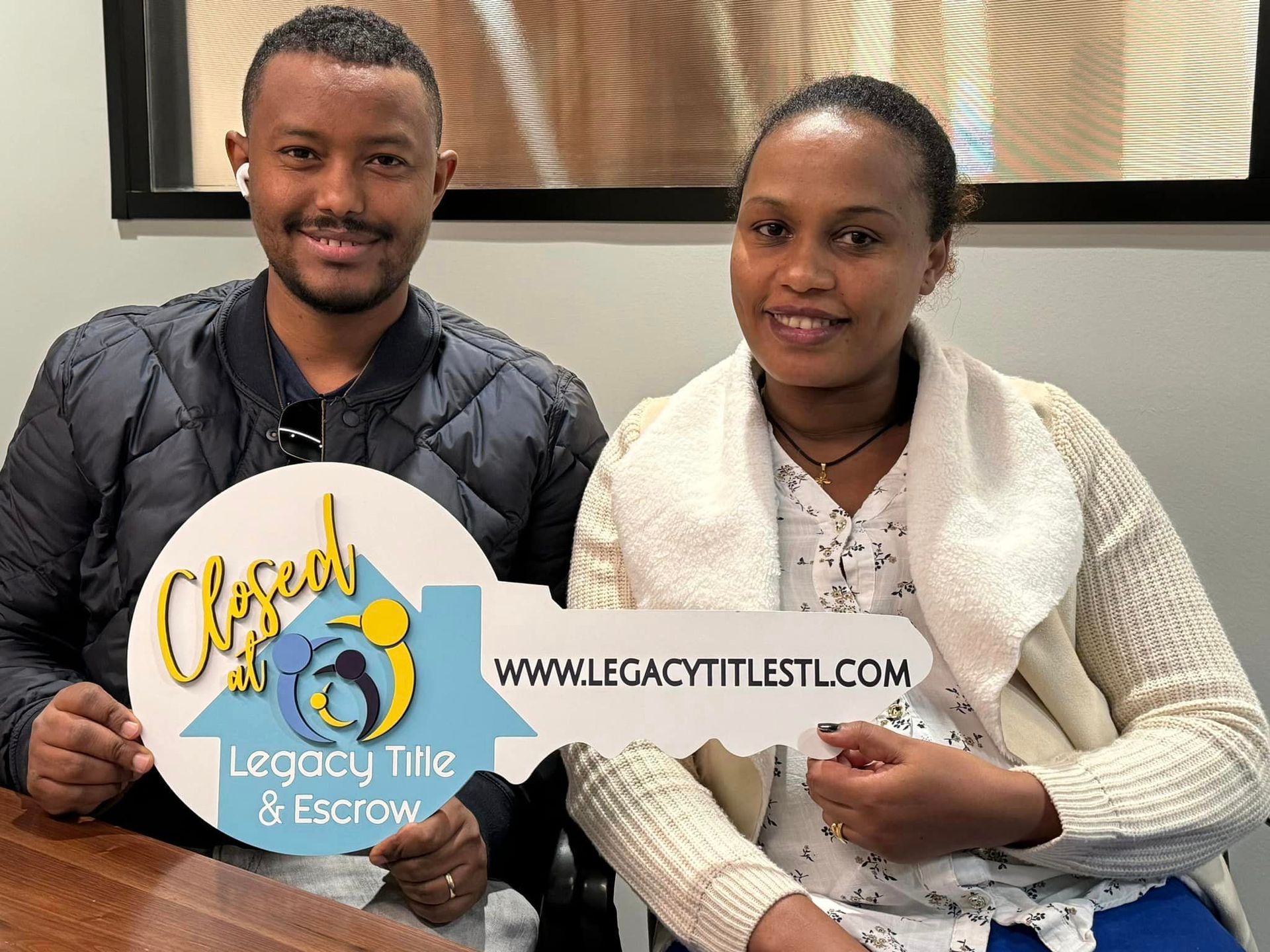 A man and a woman are sitting at a table holding keys to their new home.