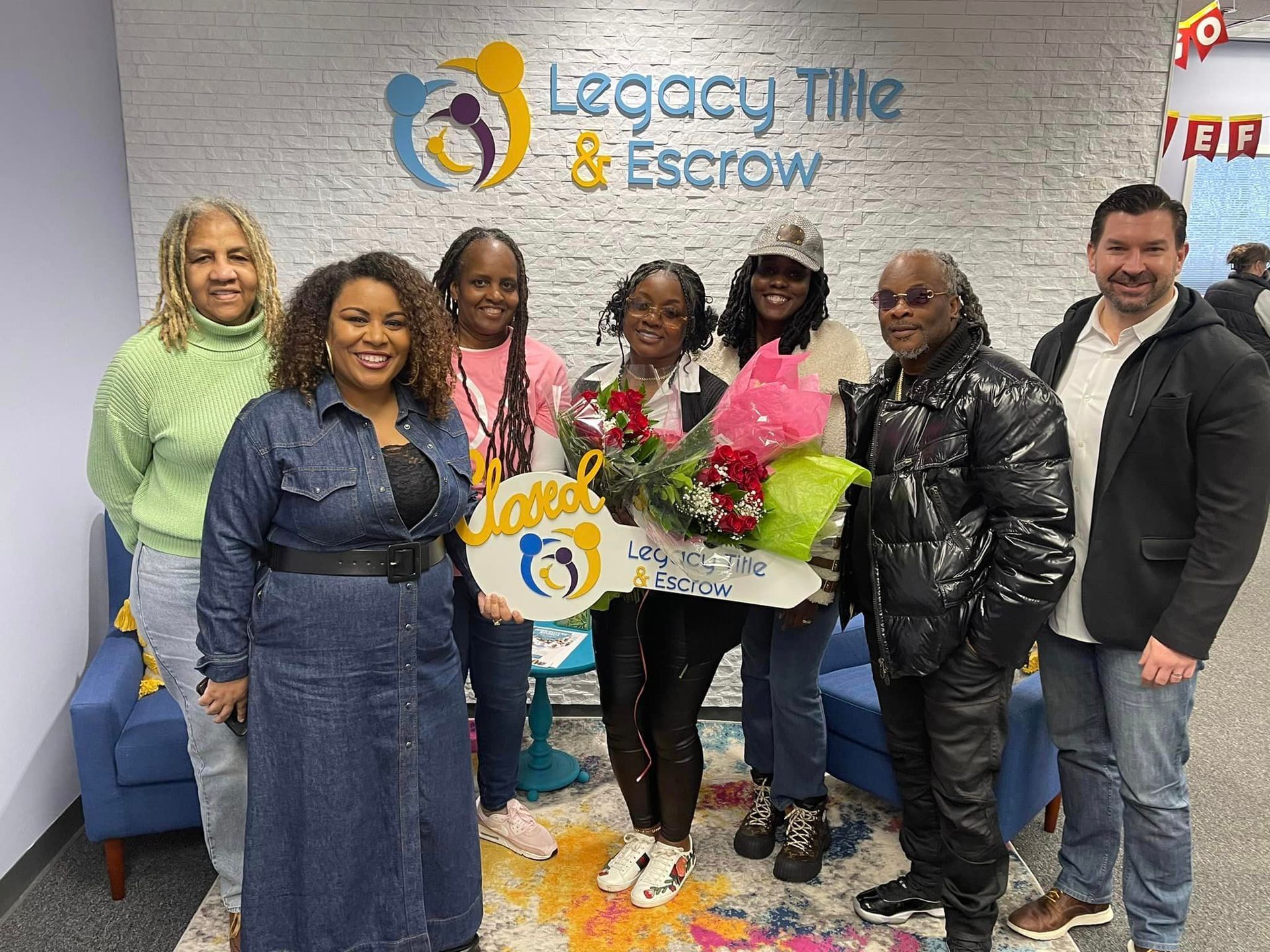 A group of people are posing for a picture in front of a legacy tile and escrow sign.