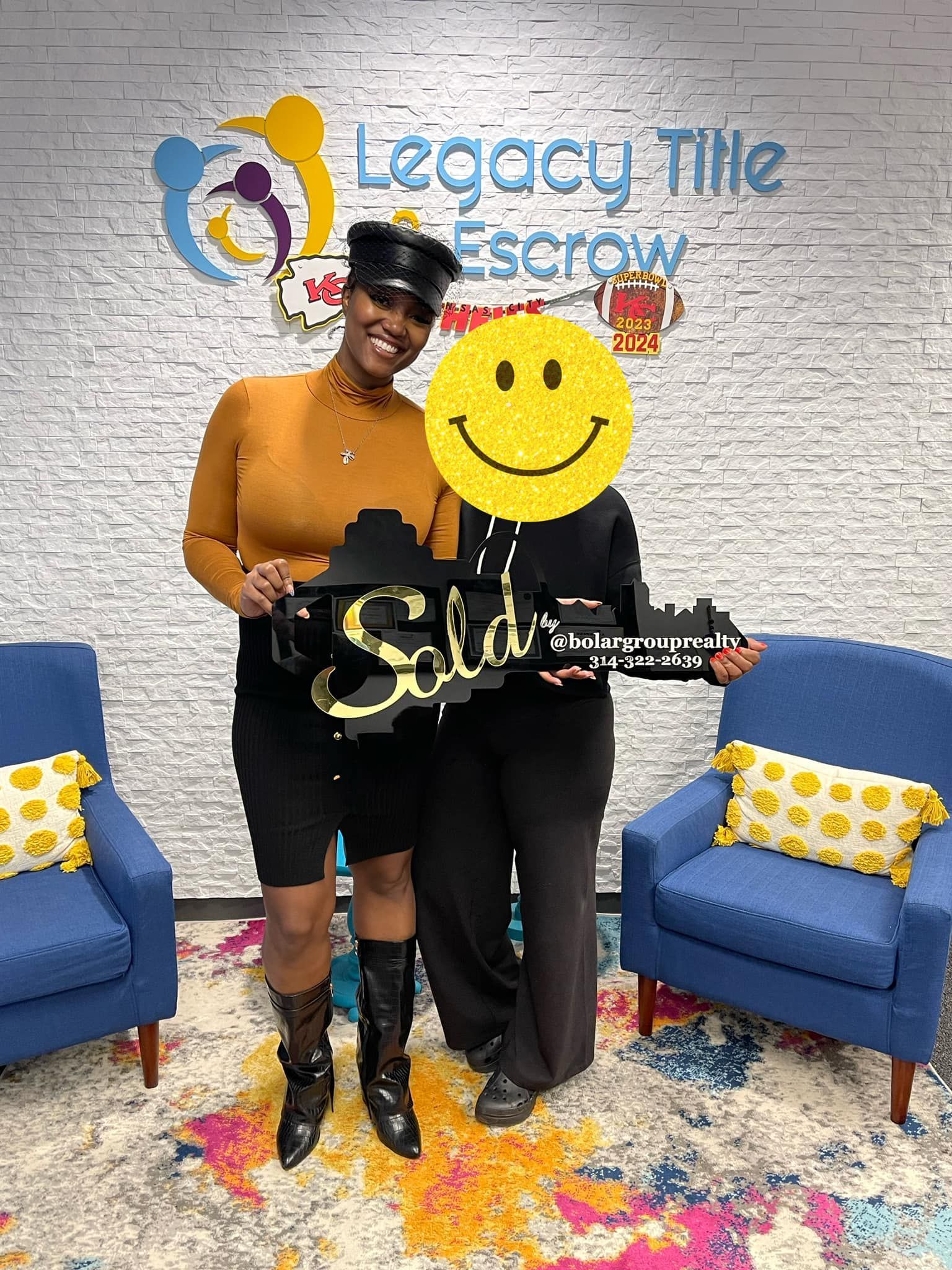 Two women are standing next to each other in a room holding a sign with a smiley face on it.