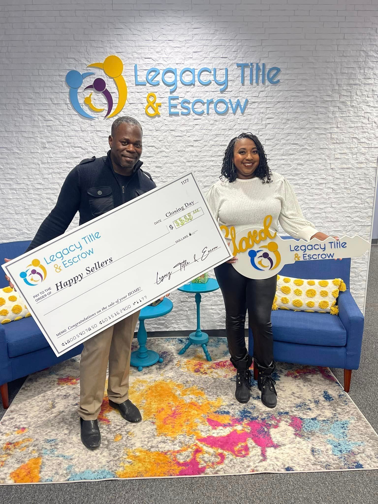A man and a woman are holding a large check in front of a brick wall.
