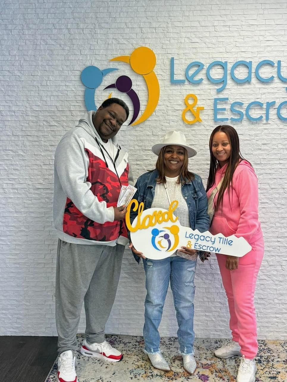 A man and two women are holding keys in front of a legacy & escrow sign.