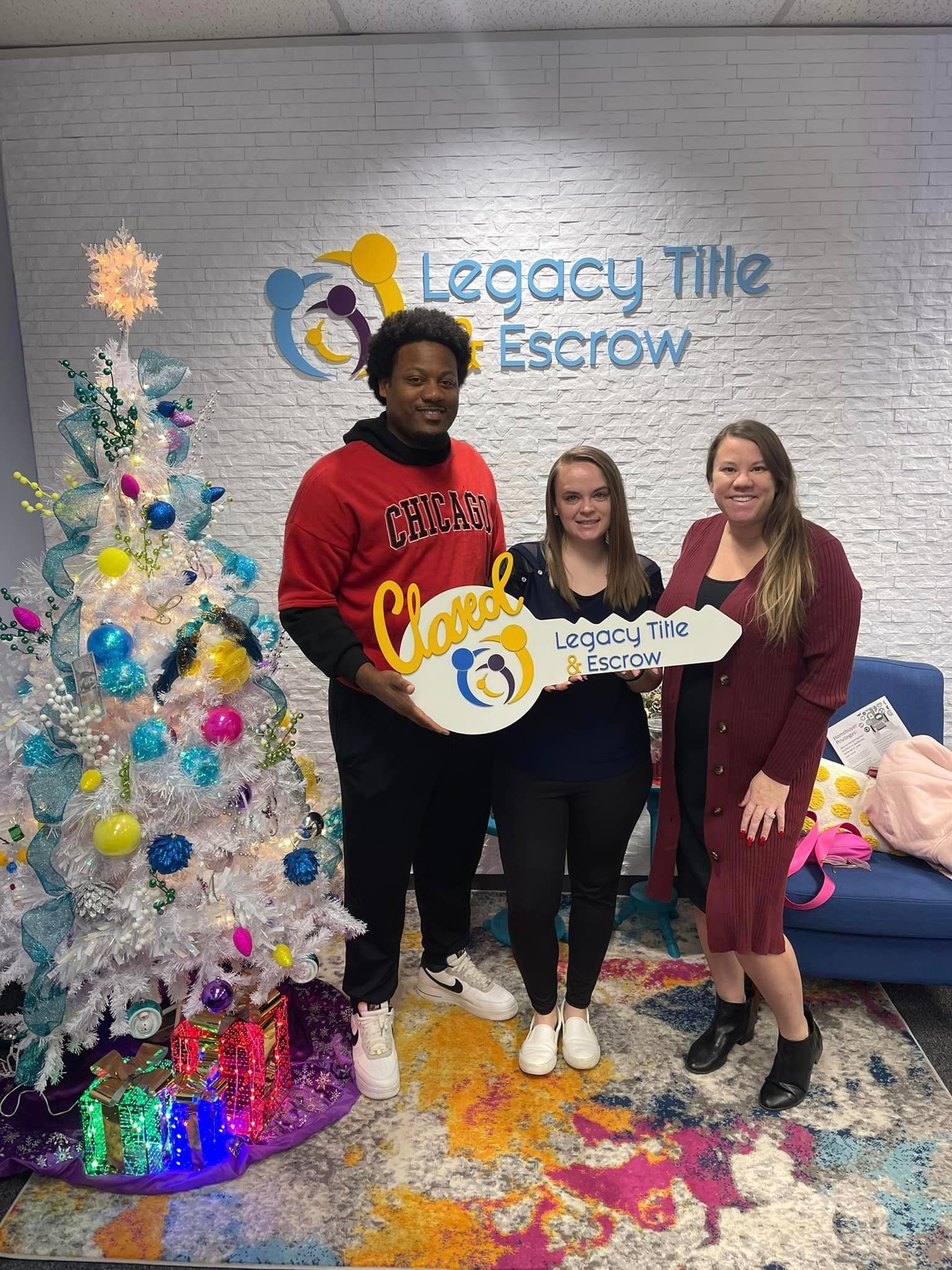 A man and two women are holding keys in front of a christmas tree.