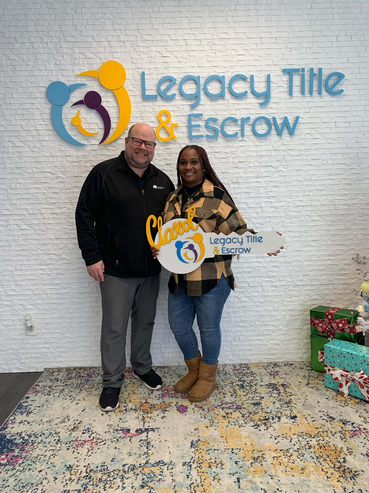 A man and a woman are standing in front of a legacy title and escrow sign holding a key.