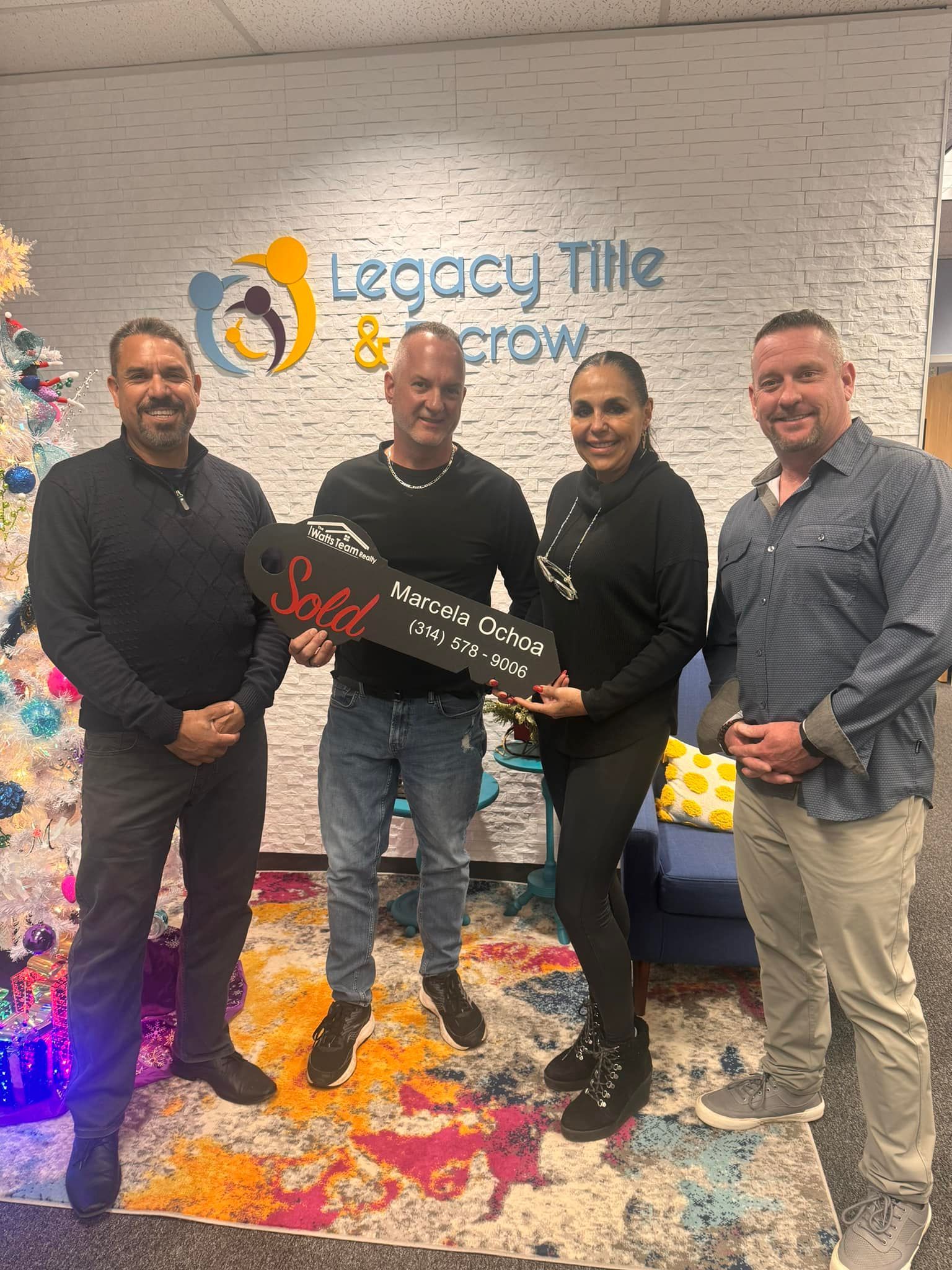 A group of people standing next to each other in front of a brick wall holding a sold sign.