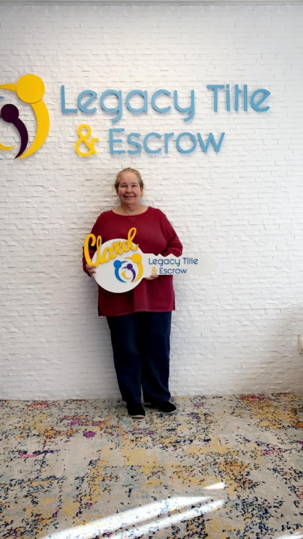 A woman is standing in front of a legacy title and escrow sign holding a key.