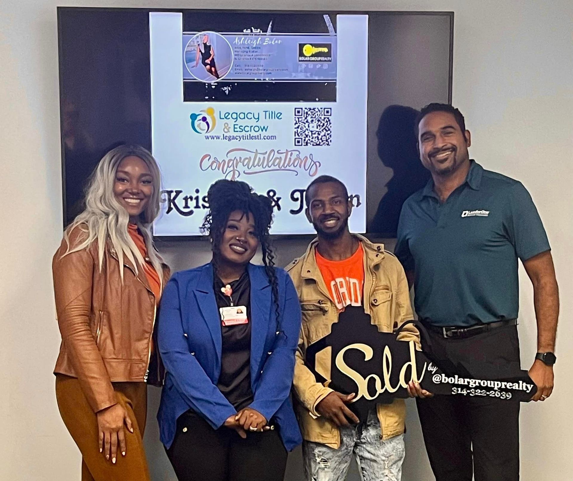 A group of people are posing for a picture in front of a sold sign.