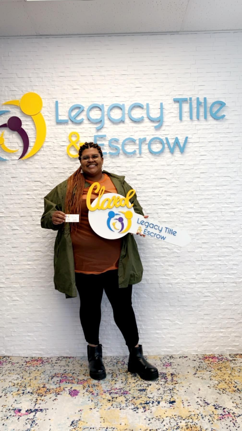 A woman is holding a key in front of a legacy title & scrow sign.