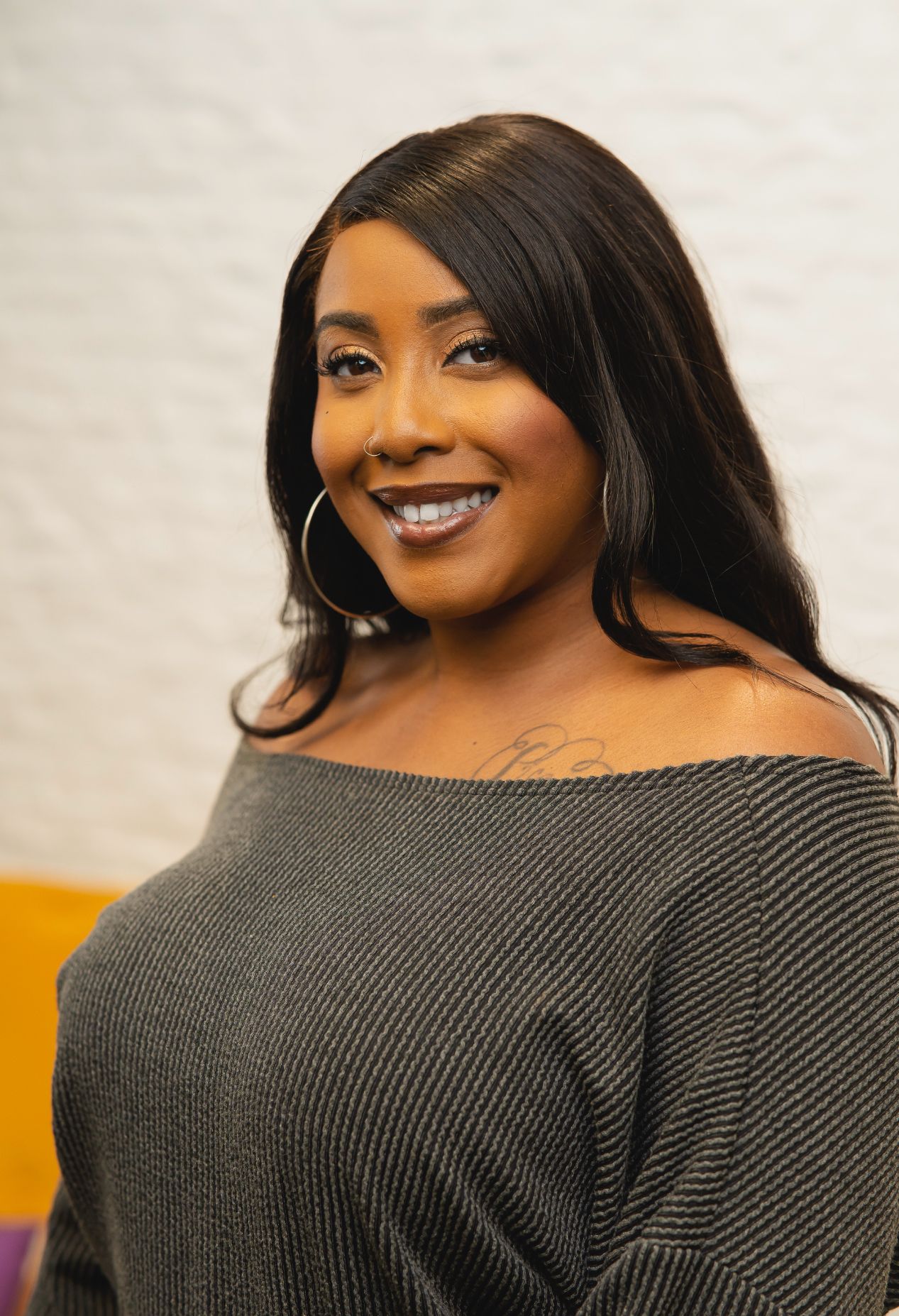 A woman in a grey off the shoulder sweater is smiling