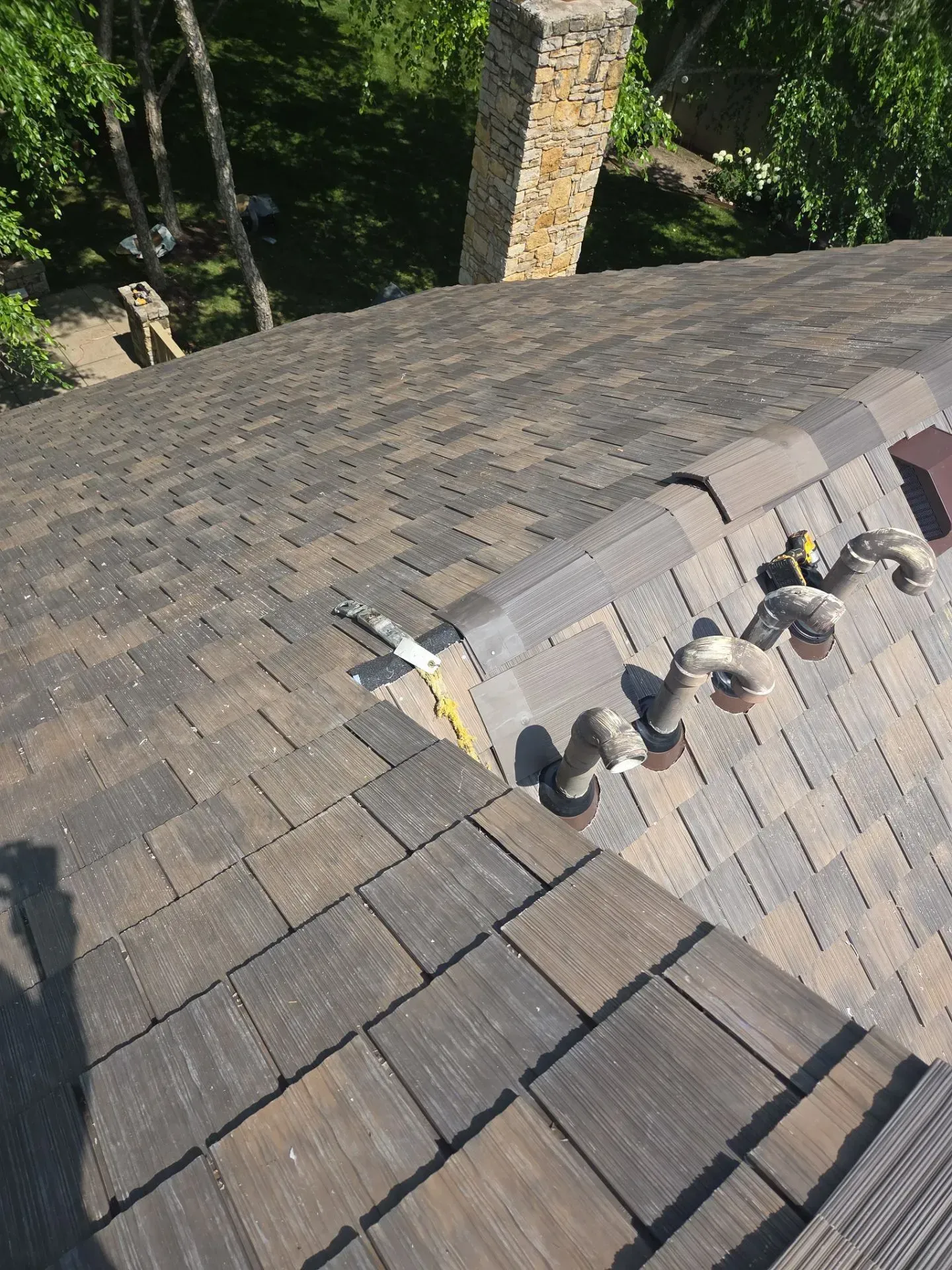 Rooftop view of shingles, pipes, and a chimney. Brown and gray hues. Sunny outdoor setting.