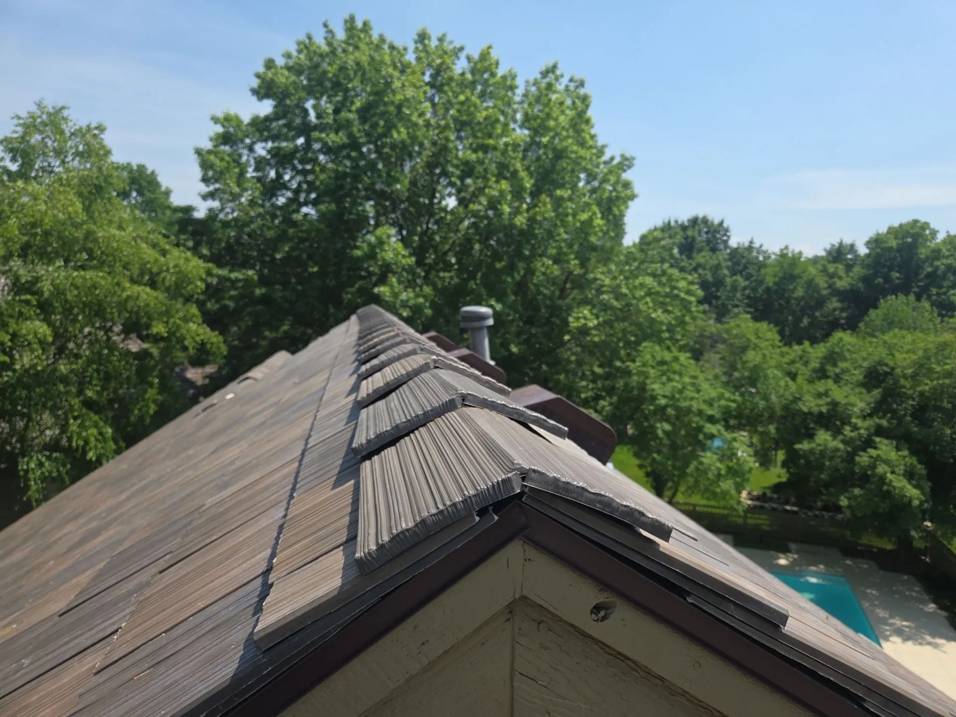 Damaged roof with missing shingles; trees and pool visible in the background on a sunny day.