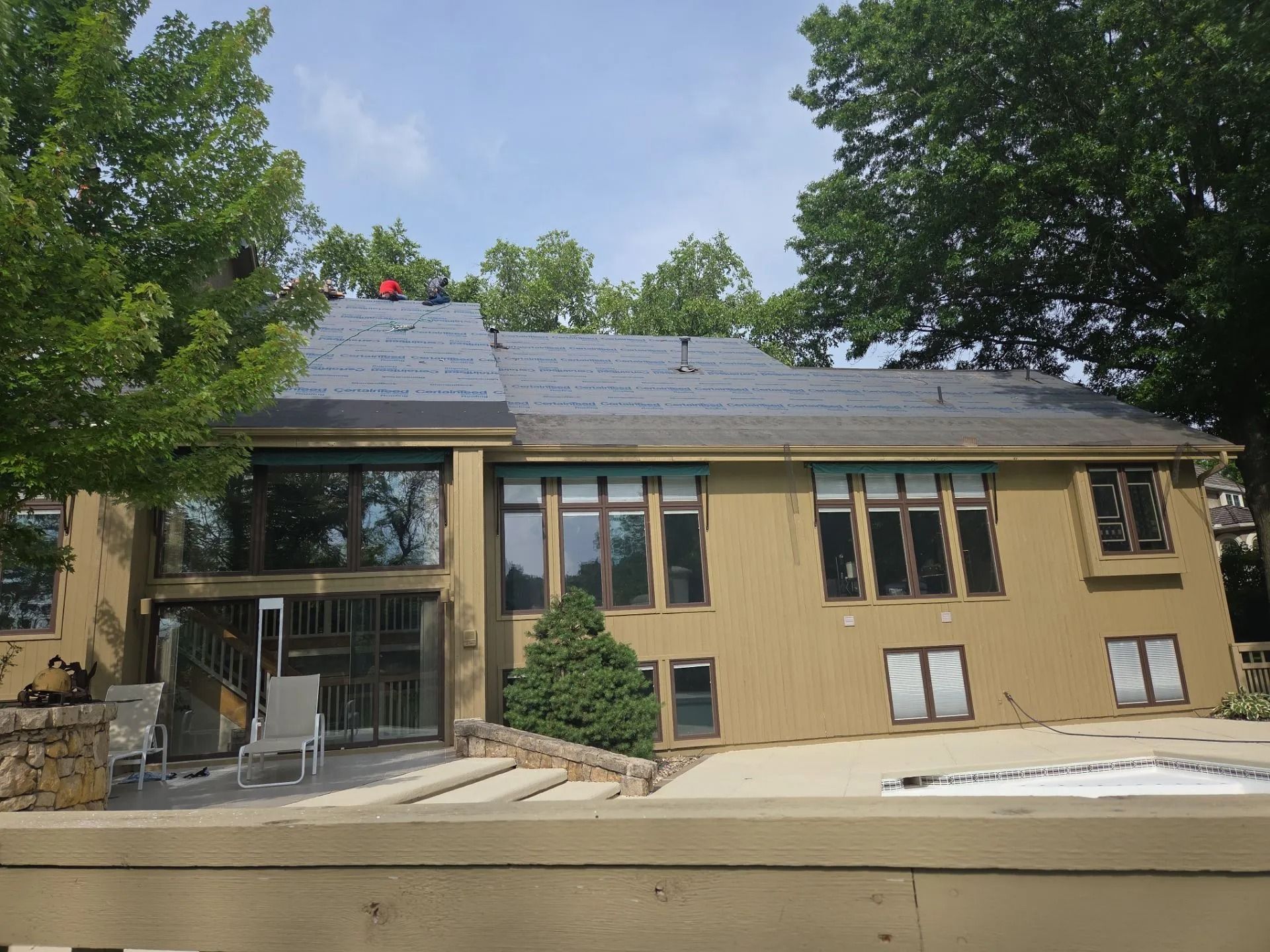 House with dark roof being worked on, large windows, and trees on sunny day.