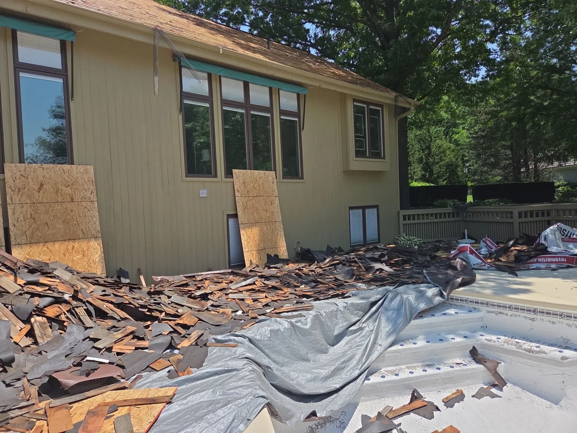 Roofing debris in a pool. House siding and windows in the background. Boards leaning against the house.