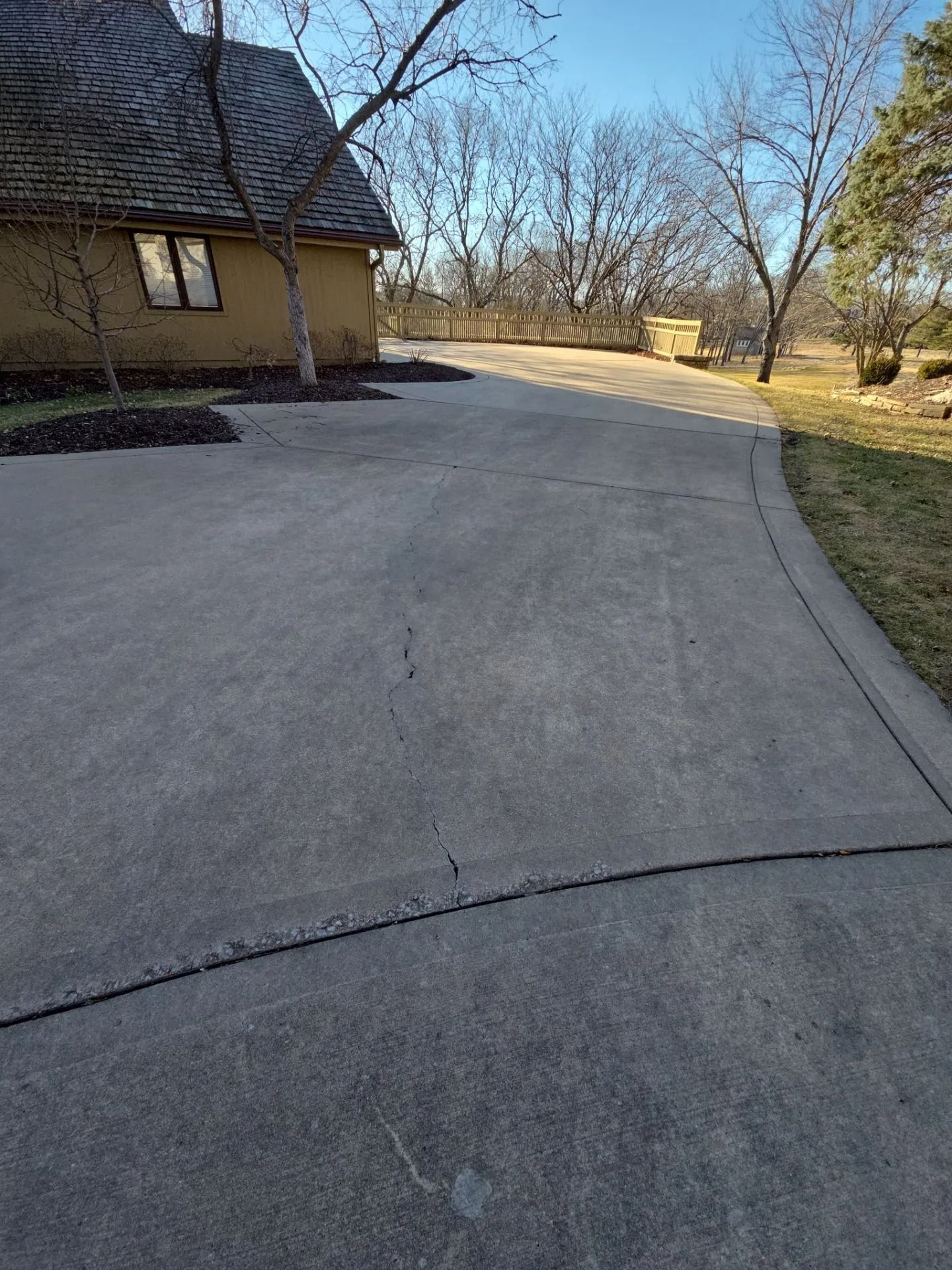 Concrete driveway curves towards a house, trees, and sky. The driveway is gray.