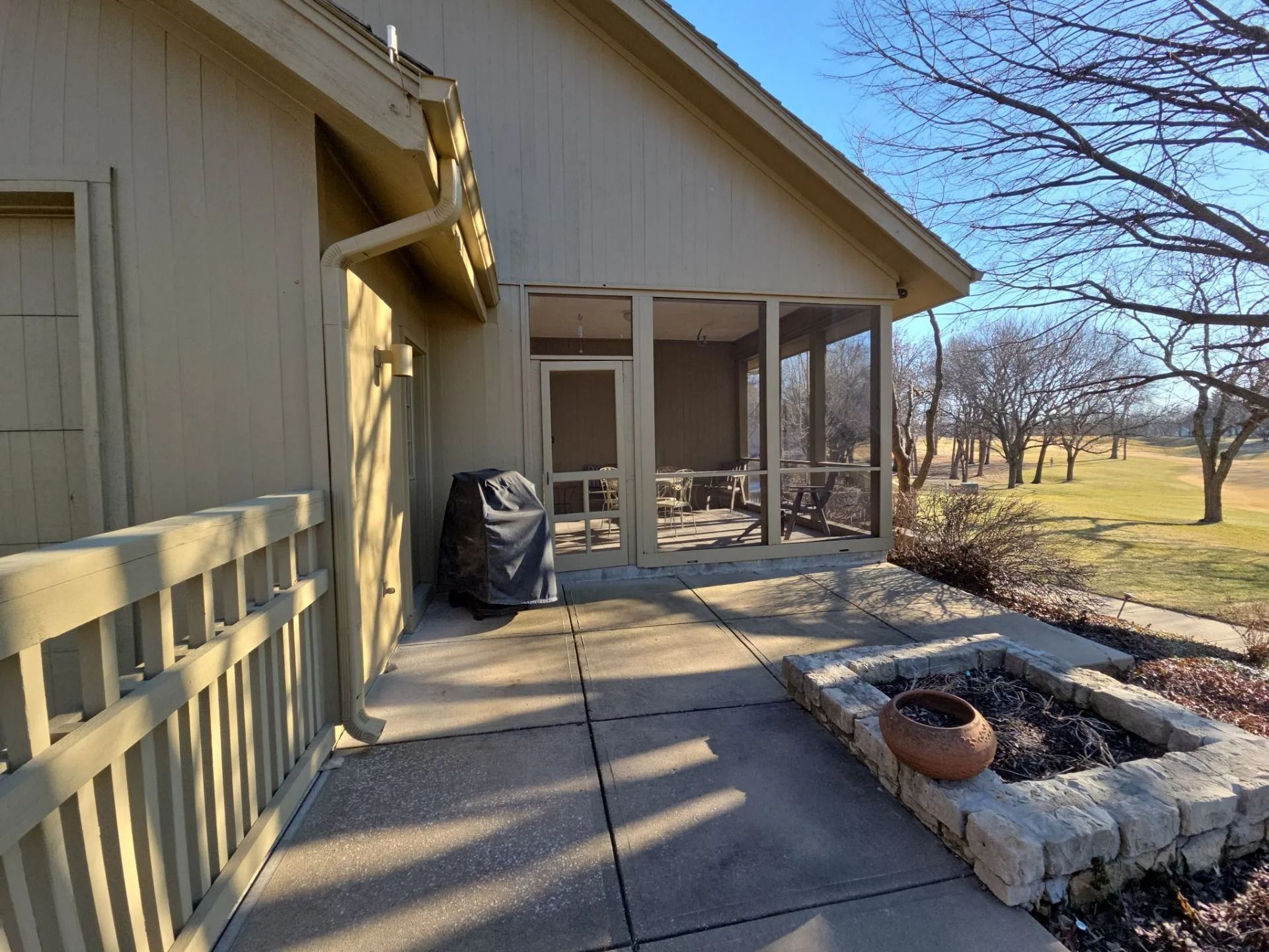 Beige house exterior with a screened porch and a view of a grassy golf course.