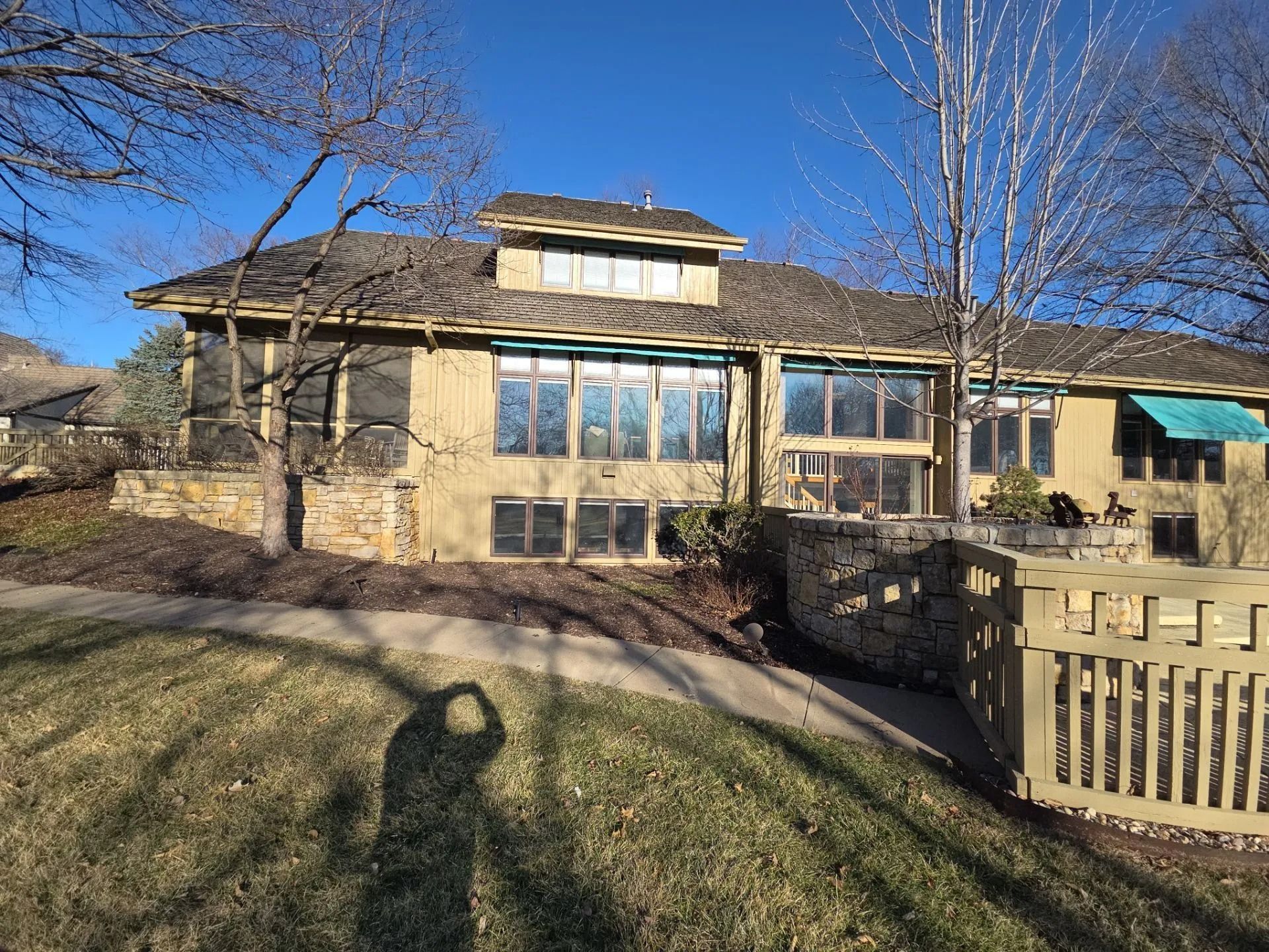 Tan house with large windows, stone accents, and a low-slung roof under a clear blue sky.