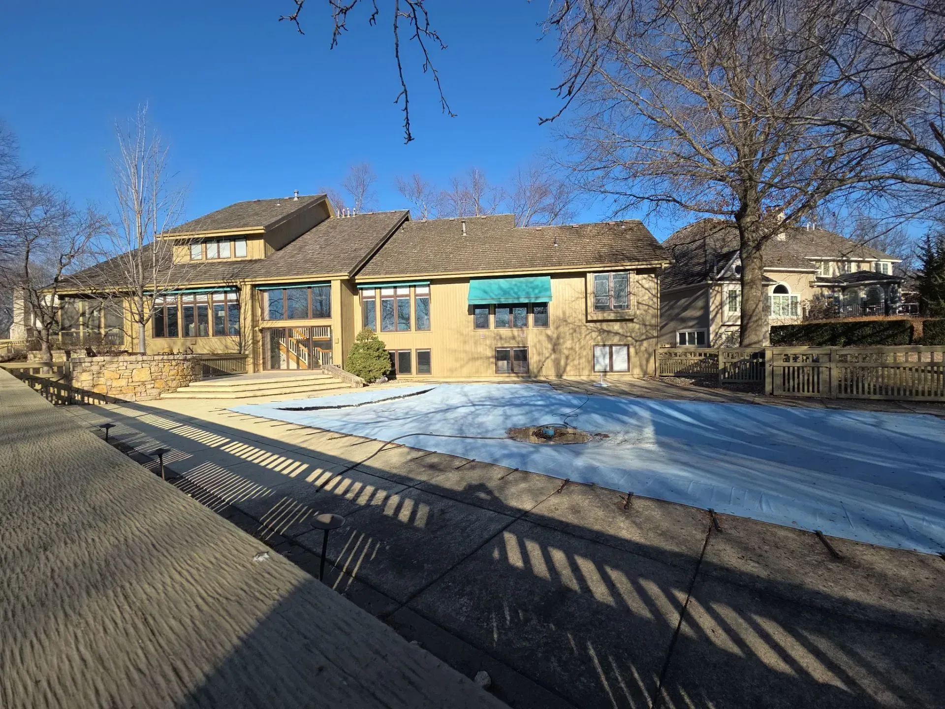 Back of a house with a pool covered by a blue tarp on a sunny day.