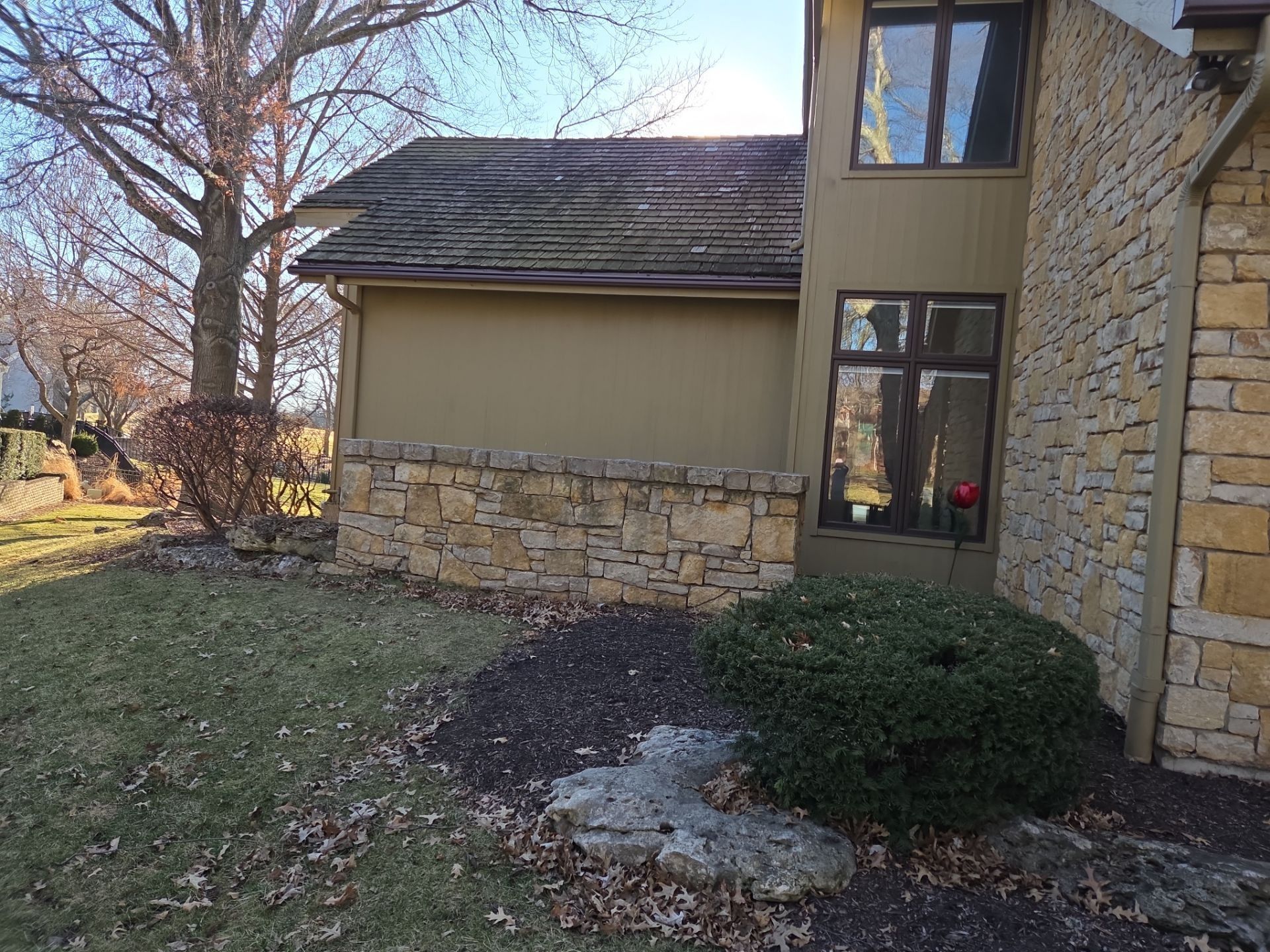 Exterior of a house with stone and tan siding, a low stone wall, and landscaping.