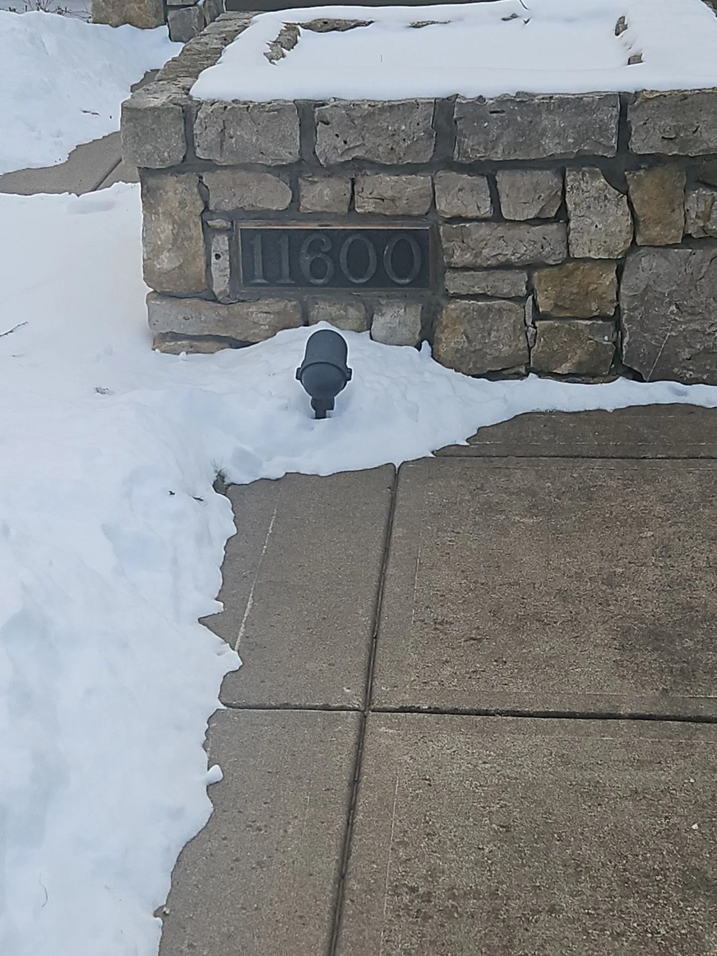 Stone wall with address 1600 in metal lettering, with snow on the ground and sidewalk.