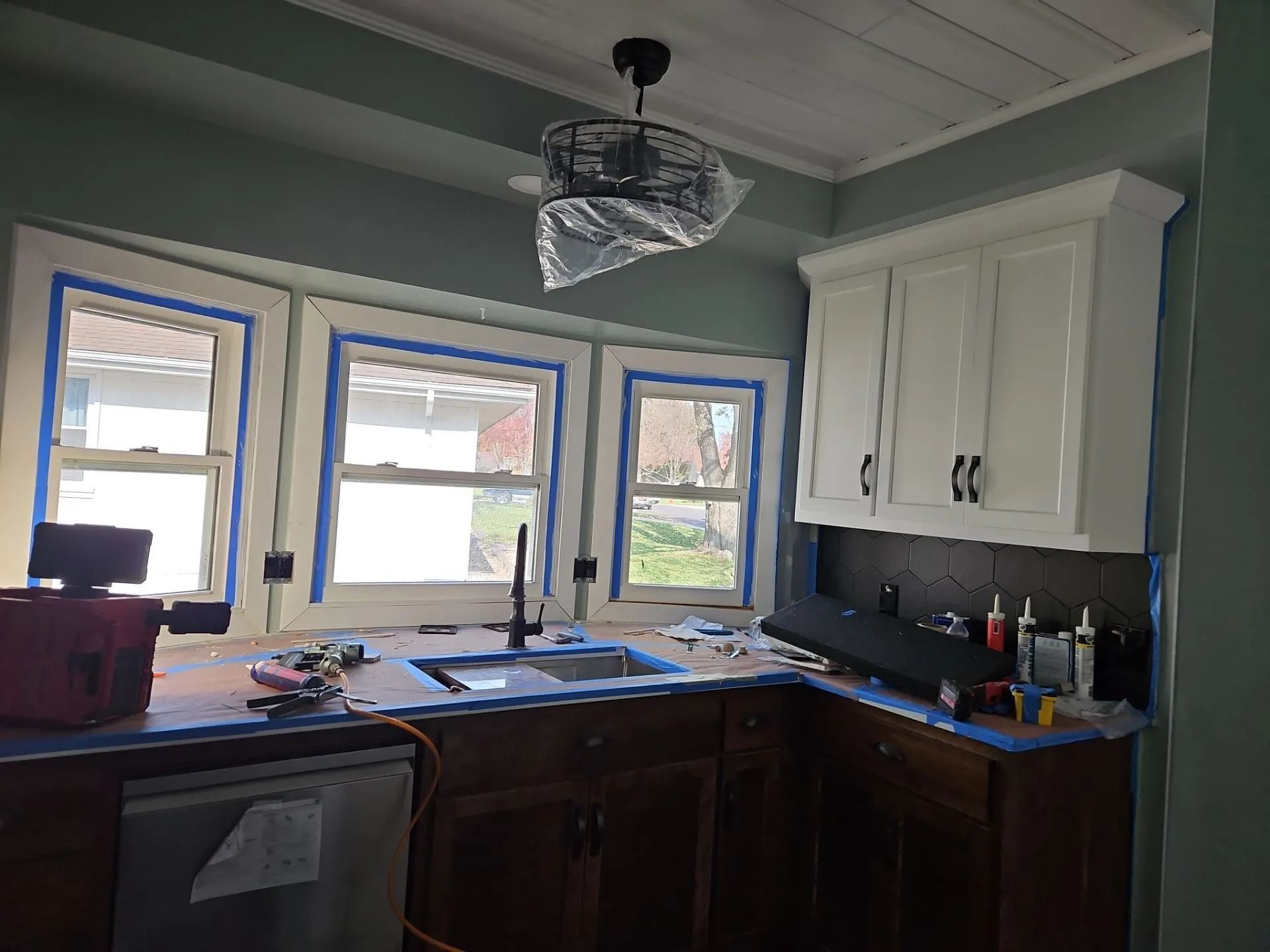 Kitchen remodel in progress, featuring new white cabinets, a sink, and three windows with blue tape.