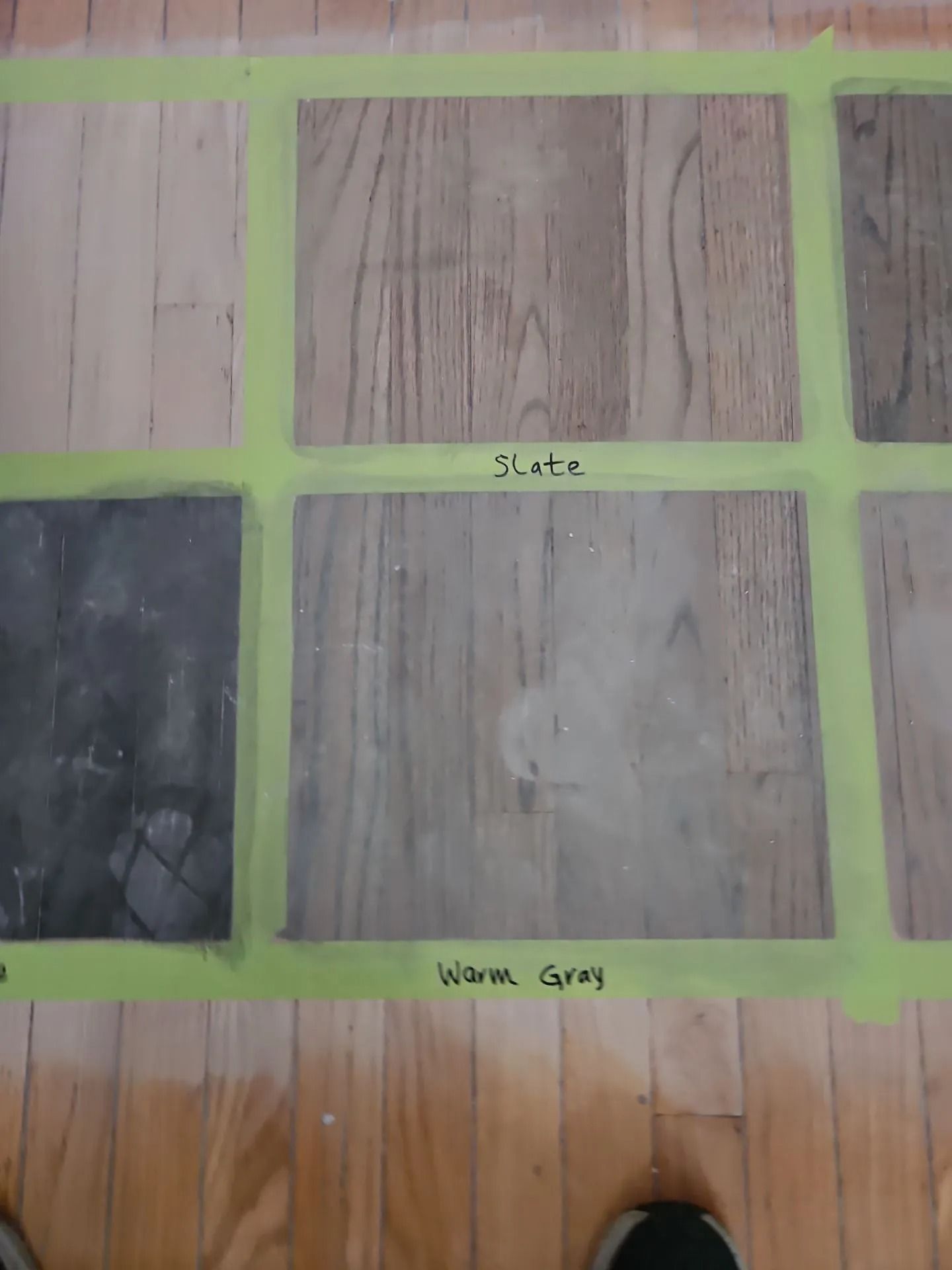 Samples of wood stain colors taped onto a wood floor: slate, warm gray, and other shades are visible.