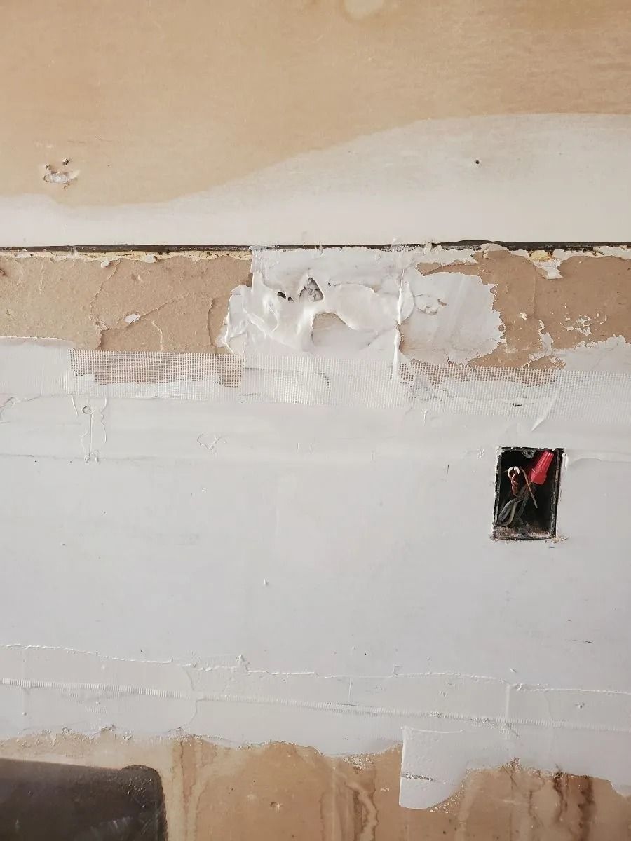 Wall under construction with exposed wood, patched drywall, and a partially open electrical box.