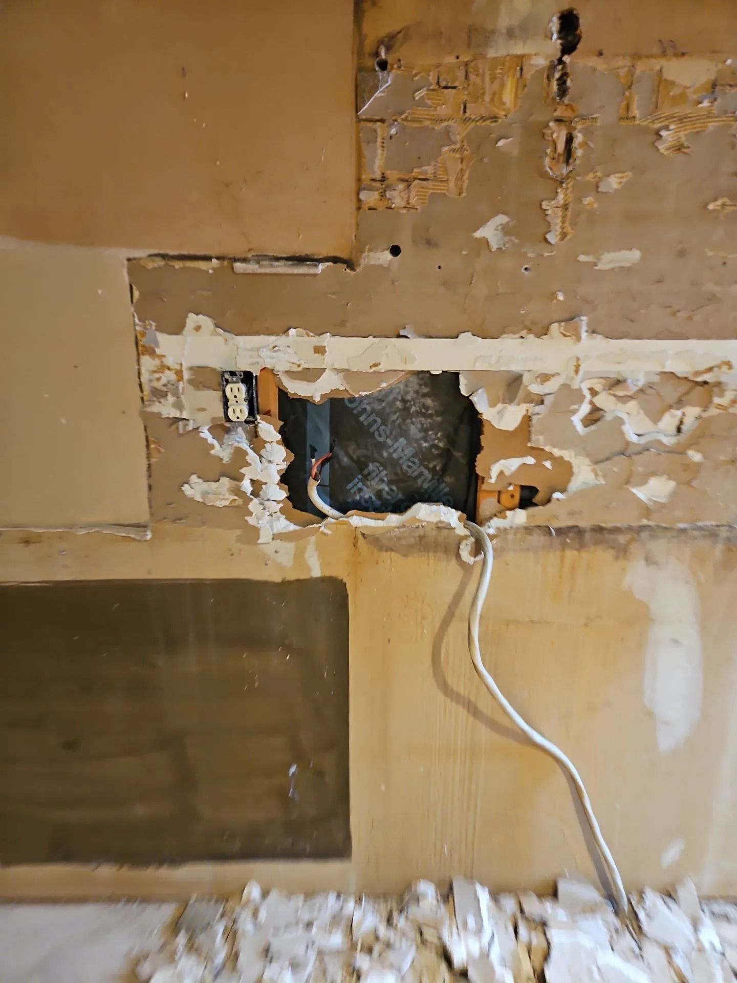 Wall with damaged plaster, exposed wiring, and electrical outlets.
