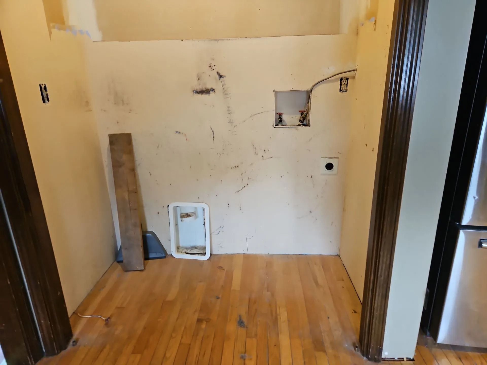 Empty utility room with wood floor, damaged walls, and an open electrical outlet.