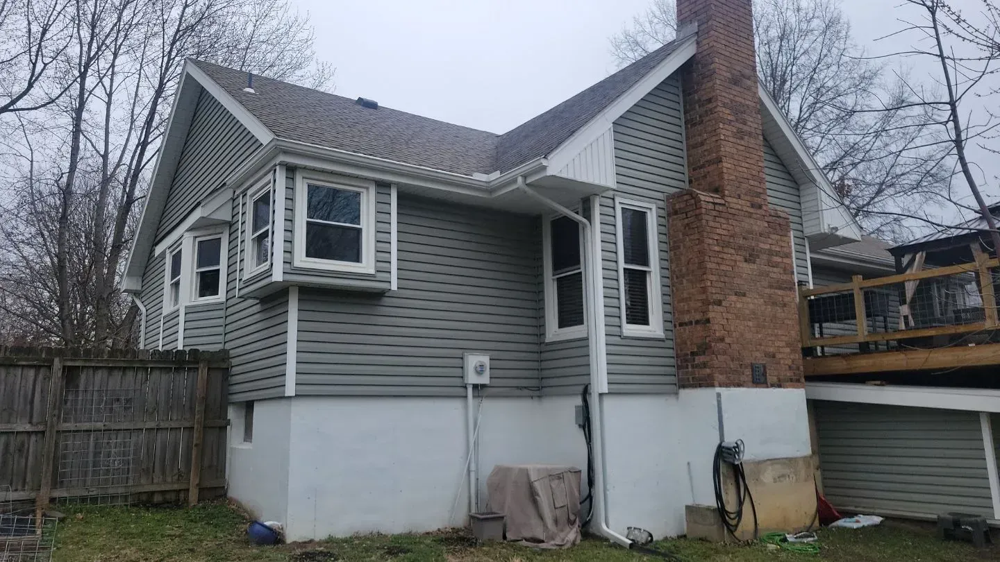 Gray house with white trim, chimney, and bay windows, under an overcast sky.