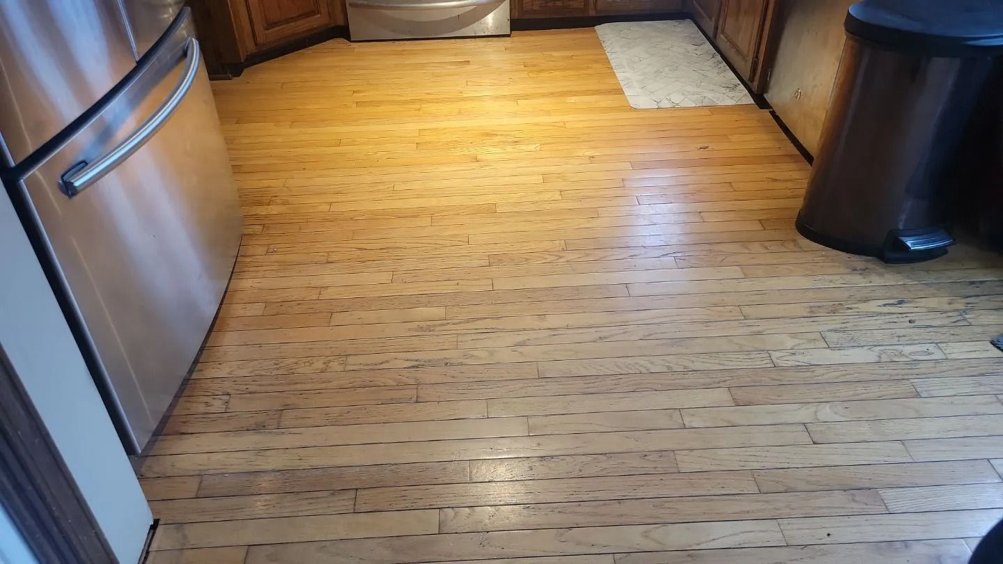 Light-colored cork flooring in a kitchen with a stainless steel appliance and a trash can.