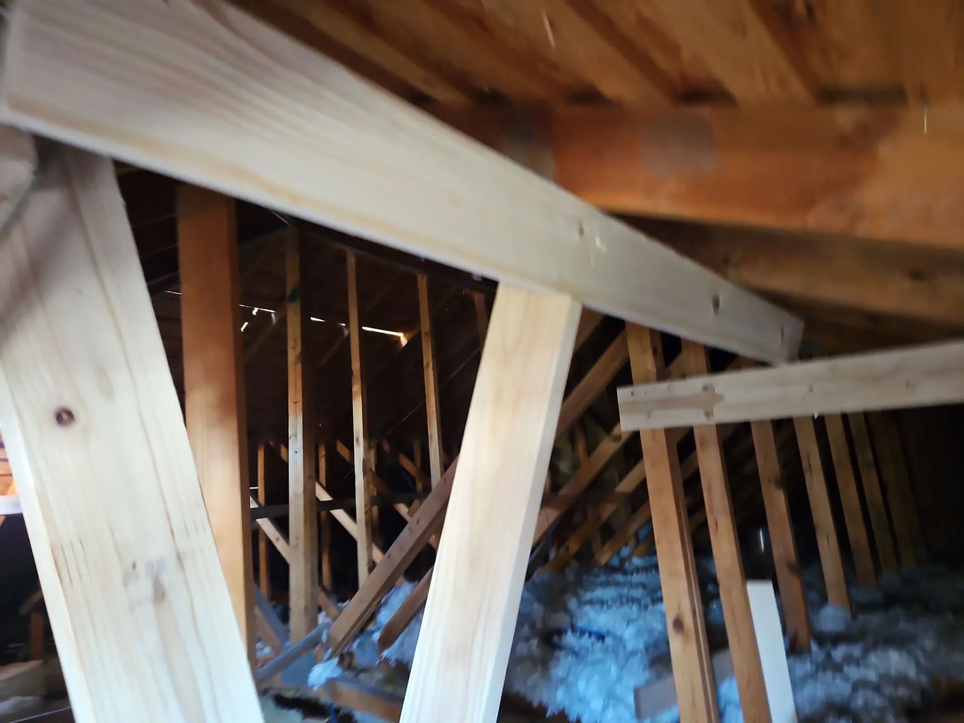 Interior view of an attic with wooden rafters and supports, some insulation visible.